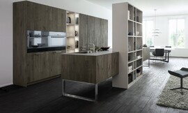 Esta cocina es una cocina de contrastes: las líneas puras de una planificación moderna y elegante se funden con lo clásico. Unos muebles de madera envejecida nudosa le otorgan autenticidad y nobleza. La estantería integrada en la isla, que dispone de un área de trabajo, fregadero y placas, actúa de perfecto elemento de transición que consigue integrar esta elegante cocina de color roble antiguo pizarra en la sala de estar. Zuordnung: Stil Cocinas clásicas, Planungsart Cocinas en L