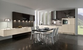 El conjunto del panel de madera con armarios altos en tonos oscuros y los armarios bajos flotantes le trasmiten a esta cocina el carácter de sala de estar. La amplia mesa, colocada en el centro de la sala, invita a disfrutar en buena compañía de ambos ambientes. Zuordnung: Stil Cocinas de diseño, Planungsart Cocinas en línea