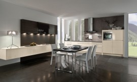El conjunto del panel de madera con armarios altos en tonos oscuros y los armarios bajos flotantes le trasmiten a esta cocina el carácter de sala de estar. La amplia mesa, colocada en el centro de la sala, invita a disfrutar en buena compañía de ambos ambientes. Zuordnung: Stil Cocinas de diseño, Planungsart Cocinas en línea