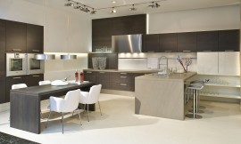 Cocina en forma de U con frentes oscuros de madera de roble. Esta cocina tiene un carácter muy especial gracias a las diferentes alturas de los armarios altos y de columna, los armarios bajos colgantes y la mezcla de materiales y colores de las diferentes áreas de trabajo. La cocina se convierte en una sala más de la casa que transmite amplitud y comodidad e invita a disfrutar de la buena compañía. Zuordnung: Stil Cocinas modernas, Planungsart Cocinas con isla