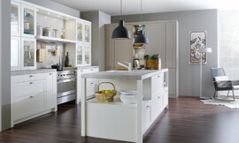 En esta cocina blanca con isla se unen elementos estéticos tradicionales a una planificación moderna centrada en la técnica y la eficiencia. Los frentes de las puertas están enmarcados, lo que le otorga ese estilo elegante, clásico y atemporal. La planificación de los diferentes elementos con un moderno equipamiento interior permite un optimo almacenamiento y un uso eficiente de la cocina que esconde las innovaciones más modernas. Zuordnung: Stil Cocinas clásicas, Planungsart Detalles del diseño