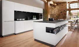 El modelo de cocina Vaso transmite una elegancia atemporal. Destaca por el contraste de colores y materiales: frentes y revestimentos de cristal blanco polar, encimera de la serie a-Top de 20 mm de grosor y chapada de roble negro y entrepaños del mismo material y color rematados con zócalo en metal .  Los revestimentos de la isla también son del mismo material. El contraste blanco y negro le da a esta cocina de diseño la elegancia y el clasicismo que desprende. Zuordnung: Stil Cocinas de diseño, Planungsart Cocinas con isla