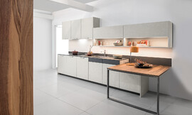 Cocina exclusiva con el frente en óptica de hormigón y mesa de extensión práctica con una superficie de alta calidad en chapa de nogal. Zuordnung: Stil Cocinas de diseño, Planungsart Cocinas en línea