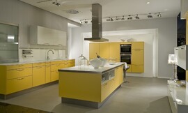 Una isla de cocina con frentes en amarillo mango y elementos, como la encimera, en blanco Zuordnung: Stil Cocinas modernas, Planungsart Cocinas en línea