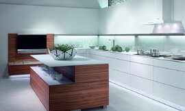 Cocina abierta de líneas puristas de Warendorf. El contraste de esta cocina en blanco puro y madera de tineo clara ayudan a asimilar dos conceptos y dos ambientes, uniendo la cocina con la sala de estar. La zona de trabajo en blanco puro, con una iluminación elegante y funcional, aparece delimitada de la zona de transición, delimitada por los frentes de madera de tineo. Zuordnung: Stil Cocinas de diseño, Planungsart Cocinas con isla