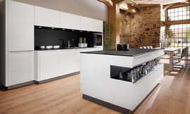 El modelo de cocina Vaso transmite una elegancia atemporal. Destaca por el contraste de colores y materiales: frentes y revestimentos de cristal blanco polar, encimera de la serie a-Top de 20 mm de grosor y chapada de roble negro y entrepaños del mismo material y color rematados con zócalo en metal .  Los revestimentos de la isla también son del mismo material. El contraste blanco y negro le da a esta cocina de diseño la elegancia y el clasicismo que desprende. Zuordnung: Stil Cocinas de diseño, Planungsart Cocinas con isla