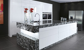 Noble, atemporal y de líneas claras. Unos muebles de cocina blancos lacados en alto brillo se ven complementados por una encimera de granito en „Black Marinace“ que más que un objeto de contraste le da un toque barroco a todo el concepto comvirtiéndose en el centro de la cocina. Zuordnung: Stil Cocinas de lujo, Planungsart Cocinas con isla