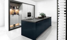 Como la noche y el día, y sin embargo, lleno de armonía: la cocina con isla en Midnight Blue ofrece un atractivo contraste con los frentes claros en Daylight Grey . En esta cocina de diseño se funde la belleza clásica y la modernidad en un todo armonioso. Los frentes con textura ondulada son muy agradables a la vista, por eso también son adecuados para cocinas rústicas. Zuordnung: Stil Cocinas de diseño, Planungsart Cocinas con isla