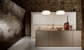 Formas geométricas y diseño minimalista. Una cocina de líneas puras que gracias a los matices y los contrastes de los diferentes materiales utilizados permiten crear una acogedora atmósfera de sala de estar. Los armarios de frentes blancos de altos brillos sin tiradores y equipados con mecanismos de apertura mecánica mediante el roce contrastan con los tonos cálidos de la encimera en cobre. La utilización de armarios de diferentes alturas rompen también la sobriedad y una iluminación pensada para crear bienestar acaban de redondear esta cocina creada para brillar en cualquier sala de estar. Zuordnung: Stil Cocinas de lujo, Planungsart Cocinas americanas (abiertas)