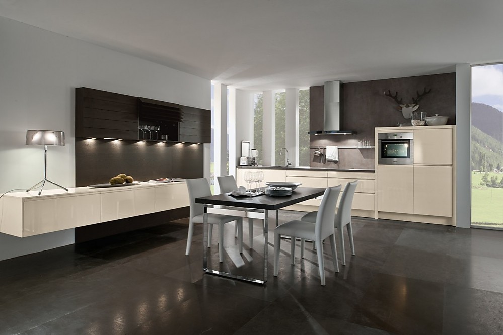 El conjunto del panel de madera con armarios altos en tonos oscuros y los armarios bajos flotantes le trasmiten a esta cocina el carácter de sala de estar. La amplia mesa, colocada en el centro de la sala, invita a disfrutar en buena compañía de ambos ambientes. Zuordnung: Stil Cocinas de diseño, Planungsart Cocinas en línea