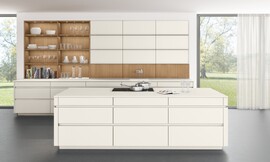 Blanca y atemporal se muestra esta cocina clásica, que sin embargo esconde grandes innovaciones. Los armarios altos que van apoyados directamente en la encimera, se dividen en compartimentos de 40 cm con puertas abatibles que permiten aprovechar todo el espacio sobre la encimera para guardar y almacenar utensilios de cocinas, libros, especias... Además la grifería o la campana van también integradas en estos elementos. La mezcla de materiales y colores , frentes lacados en blanco mate con frentes de madera de roble cobrizo le dan un toque personal de elegancia a esta cocina con isla. Zuordnung: Stil Cocinas de diseño, Planungsart Detalles del diseño