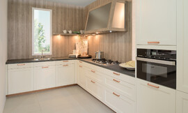 ¿Quieres una cocina rústica acogedora con elementos nobles? Esta cocina en forma de L provoca en cualquier espacio un ambiente acogedor con ese algo especial.  Los frentes enmarcados lacados en magnolia claro son muy acogedores y se han equipado con tiradores de color cobre realzando la alta calidad del conjunto. Zuordnung: Stil Cocinas de diseño, Planungsart Cocinas en línea