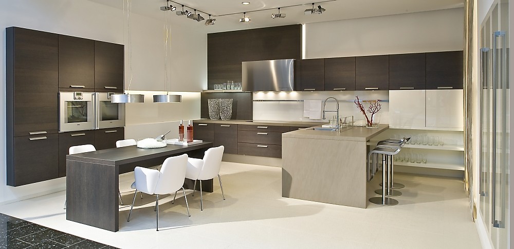 Cocina en forma de U con frentes oscuros de madera de roble. Esta cocina tiene un carácter muy especial gracias a las diferentes alturas de los armarios altos y de columna, los armarios bajos colgantes y la mezcla de materiales y colores de las diferentes áreas de trabajo. La cocina se convierte en una sala más de la casa que transmite amplitud y comodidad e invita a disfrutar de la buena compañía. Zuordnung: Stil Cocinas modernas, Planungsart Cocinas en U