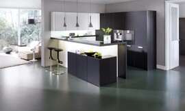 Los costados, la barra y el entrepaño son del mismo material negro que la encimera, lo que le da continuidad al conjunto y contrasta con los frentes de cristal blanco mate de los armarios bajos. La gran protagonista de esta cocina es la encimera de Corian de 13 mm de espesor. Zuordnung: Stil Cocinas modernas, Planungsart Cocinas americanas (abiertas)