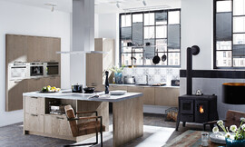 Esta cocina con isla y barra en Oak Line es un símbolo del confort. El frente de madera de roble claro en colores pastel Grey envuelve la habitación inmediatamente con calidez y confort. Zuordnung: Stil Cocinas de diseño, Planungsart Cocinas con isla